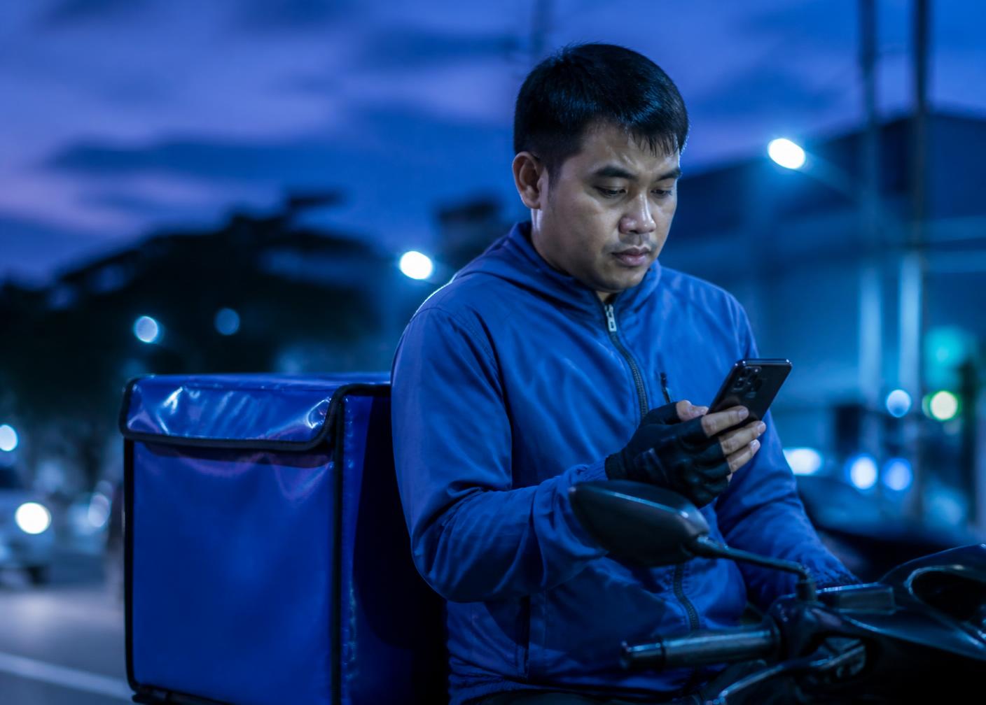 A delivery rider checking an assignment on his phone on a Philippine street at dusk